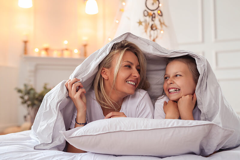 Happy mother and young daughter lying on their stomachs under a blanket